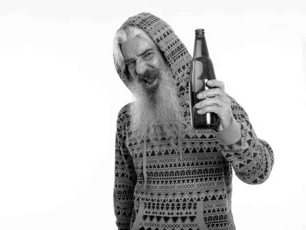 Estudio de tiro de hombre barbudo alto feliz sonriendo y usando sudadera con capucha mientras sostiene la botella de cerveza —  Fotos de Stock