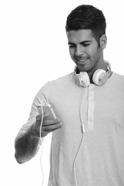 Junger glücklicher persischer Mann lächelt und benutzt Handy, während er Kopfhörer um den Hals trägt — Stockfoto