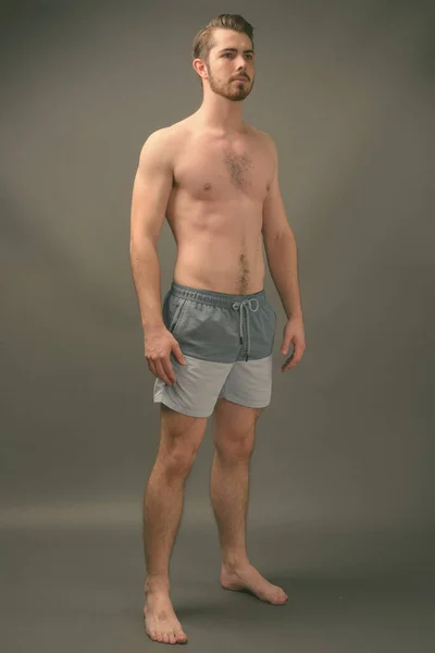 Junger gutaussehender bärtiger Mann ohne Hemd vor grauem Hintergrund — Stockfoto