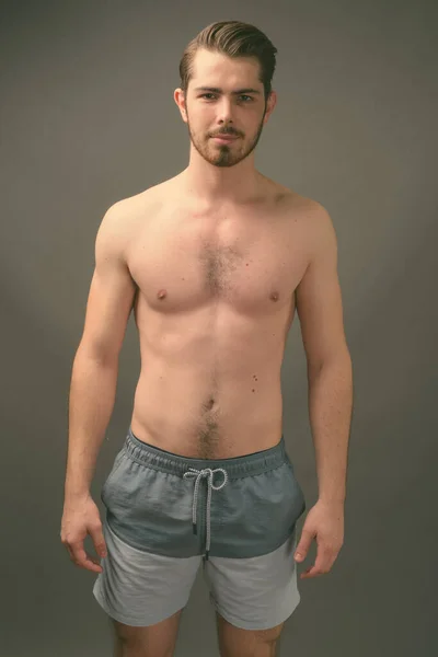 Mladý pohledný vousatý muž bez košile proti šedému pozadí — Stock fotografie