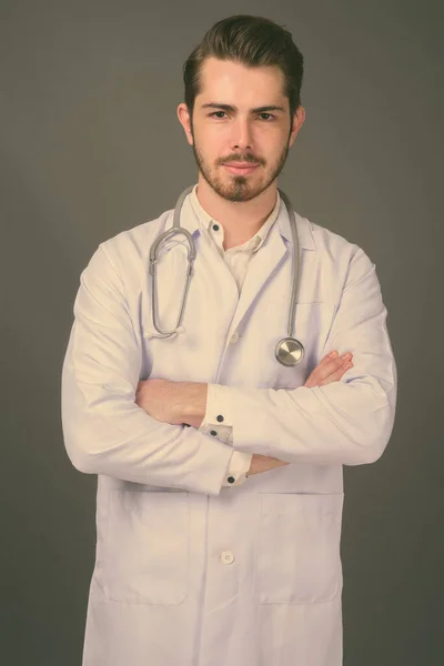 Jovem bonito barbudo homem médico contra fundo cinza — Fotografia de Stock