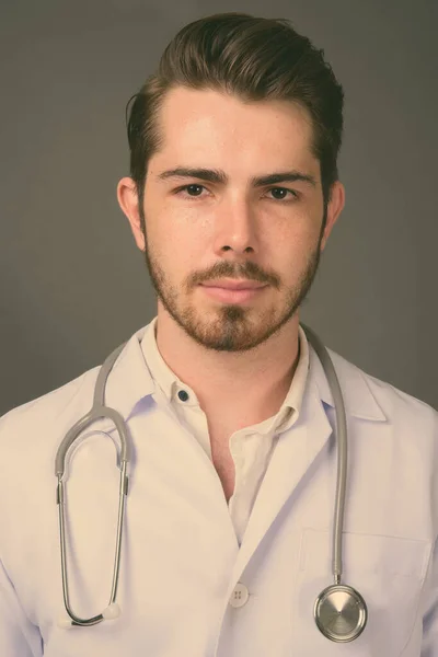Jonge knappe bebaarde man arts tegen grijze achtergrond — Stockfoto