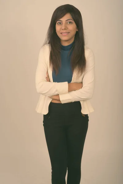 Studio shot di giovane donna d'affari persiana felice sorridente mentre in piedi con le braccia incrociate sullo sfondo grigio — Foto Stock