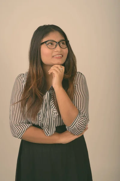 Estudio de la joven feliz mujer de negocios persa gorda sonriendo mientras piensa y usa anteojos contra el fondo gris —  Fotos de Stock