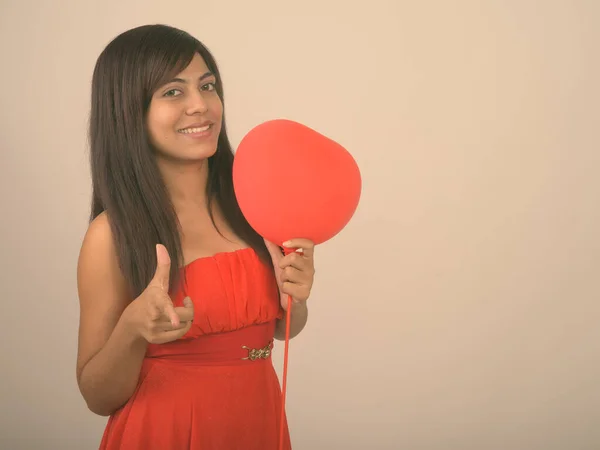 Genç mutlu İranlı kadın kameraya bakıp gülümsüyor ve elinde sevgililer gününe hazır kırmızı kalp şeklinde bir balon tutuyor. — Stok fotoğraf