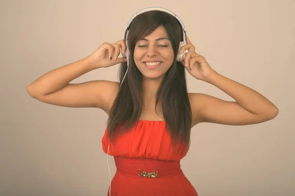 Estúdio tiro de jovem feliz mulher persa sorrindo enquanto ouve música com os olhos fechados contra fundo cinza — Fotografia de Stock