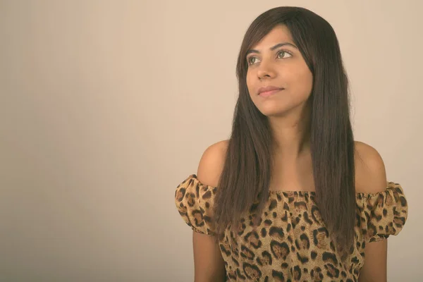 Close up of young Persian woman thinking and looking up against gray background