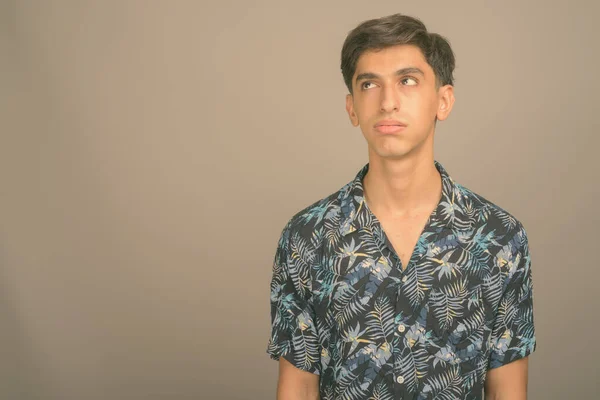 Giovane bel ragazzo adolescente persiano che indossa camicia hawaiana contro sfondo grigio — Foto Stock