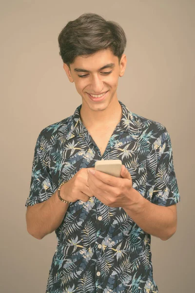 Giovane bel ragazzo adolescente persiano che indossa camicia hawaiana contro sfondo grigio — Foto Stock