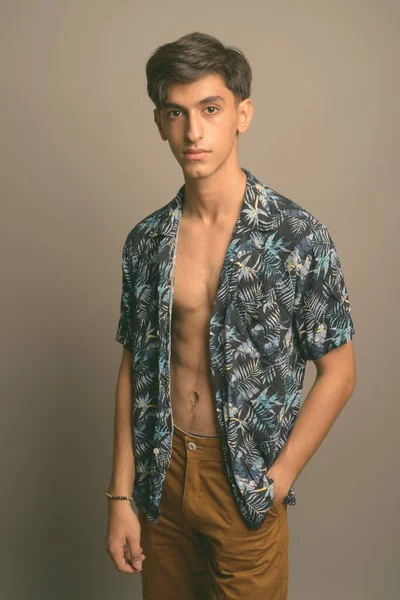 若いですハンサムなペルシャのティーン男の子身に着けていますハワイアンシャツに対してグレー背景 — ストック写真