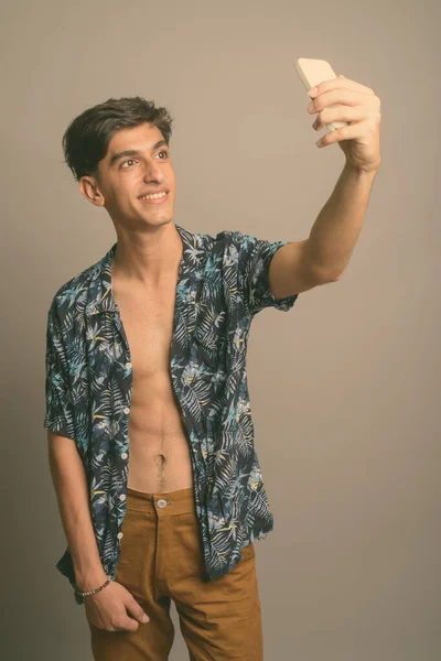 Mladý pohledný perský dospívající chlapec na sobě havajské tričko proti šedému pozadí — Stock fotografie
