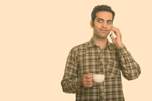 Jonge Perzische man praten op mobiele telefoon terwijl het houden van koffie kopje — Stockfoto
