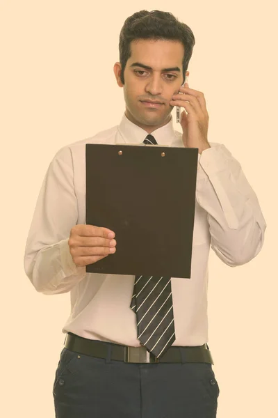 Young Persian businessman talking on mobile phone and reading clipboard — Stock Photo, Image