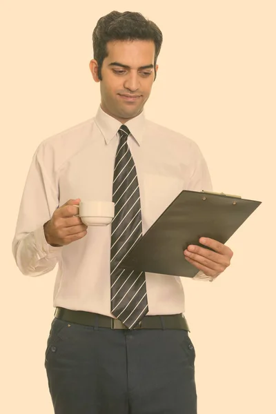 Young Persian businessman reading clipboard while holding coffee cup — Stock Photo, Image