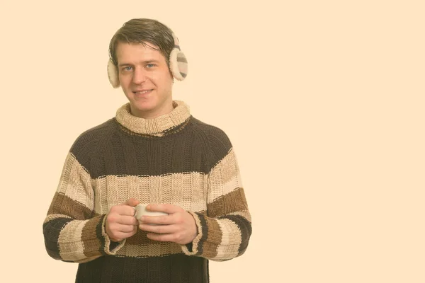 Feliz hombre caucásico guapo usando orejeras de invierno y sosteniendo la taza de café —  Fotos de Stock