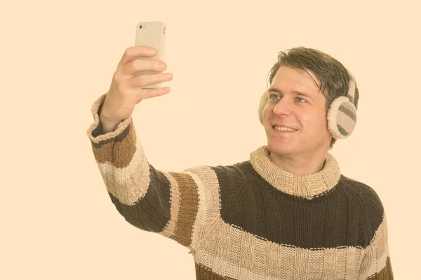 Feliz hombre caucásico guapo usando orejeras de invierno y tomando selfie con teléfono móvil —  Fotos de Stock