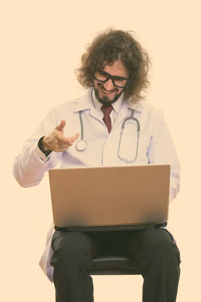 Студийный снимок счастливого врача, улыбающегося во время использования и указывающего на ноутбук — стоковое фото