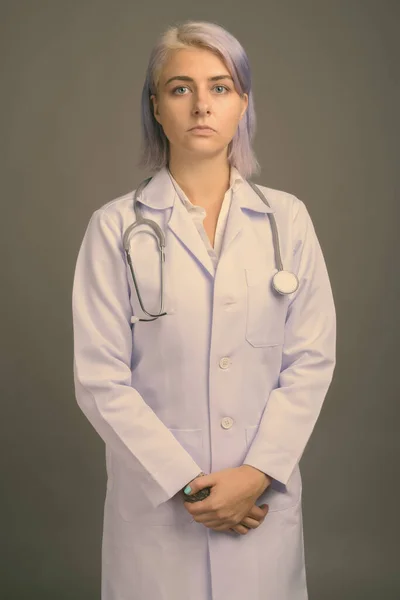 Молодая красивая женщина врач с короткими красочными волосами на сером фоне — стоковое фото