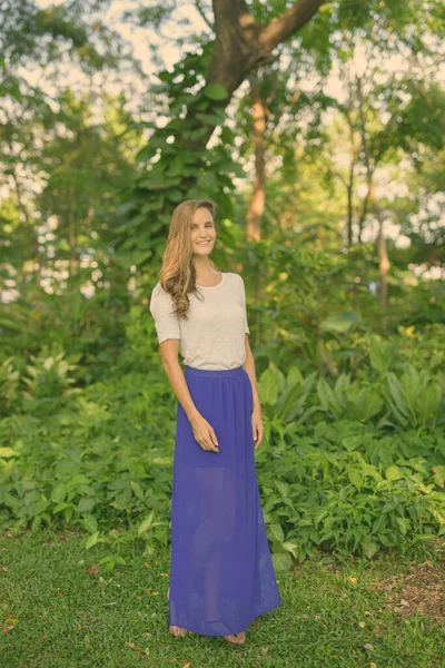 Volledig lichaam schot van gelukkige mooie vrouw glimlachend terwijl staan tegen schilderachtige uitzicht op gezonde groene tuin in het park — Stockfoto