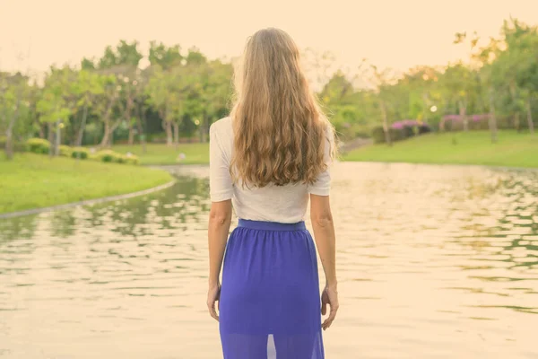 Hermosa mujer con el pelo largo de pie y mirando a la vista panorámica del lago en el tranquilo parque verde —  Fotos de Stock