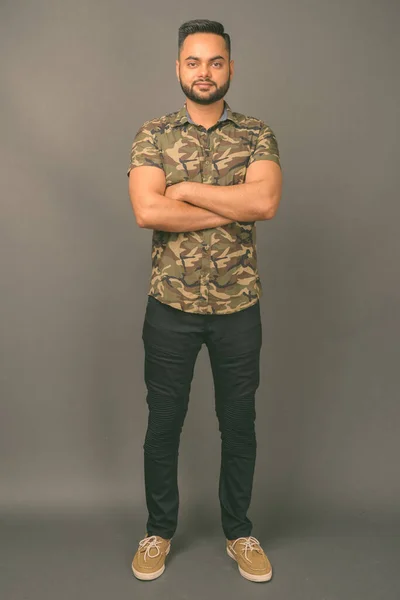 Young bearded Indian man against gray background