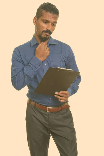 Junger indischer Geschäftsmann liest Klemmbrett beim Nachdenken — Stockfoto