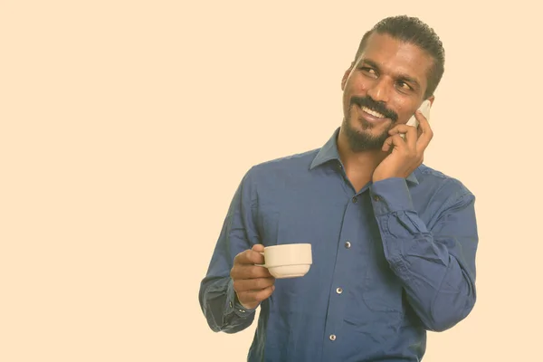 年轻快乐的印度商人一边一边拿着咖啡杯一边用手机聊天 — 图库照片