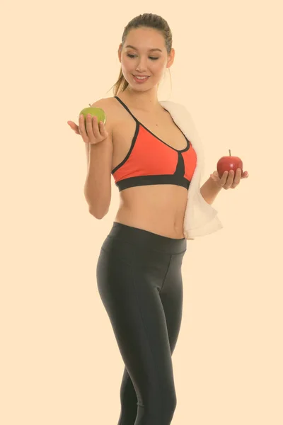 Studio zdjęcie młodej szczęśliwej pięknej Azjatki uśmiechniętej i stojącej trzymając czerwone jabłko i patrząc na zielone jabłko — Zdjęcie stockowe