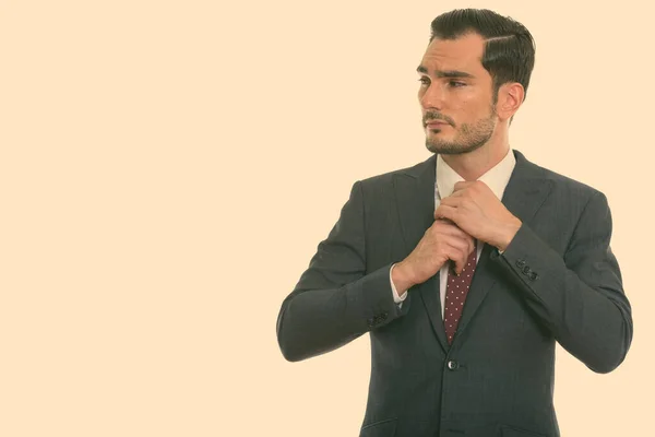 Studio shot van jonge knappe zakenman denken en weg te kijken terwijl de vaststelling van zijn stropdas — Stockfoto