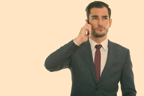 Studio shot van jonge knappe zakenman denken tijdens het praten op mobiele telefoon — Stockfoto