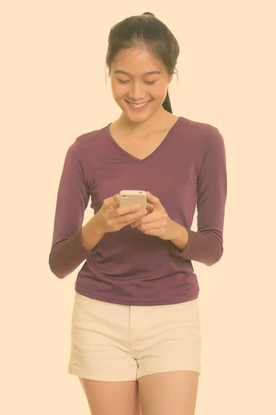 Joven feliz asiática adolescente sonriendo y usando el teléfono móvil — Foto de Stock