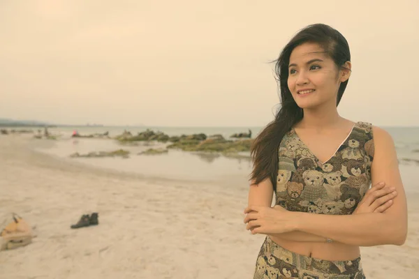 Joven feliz hermosa mujer asiática sonriendo mientras piensa con los brazos cruzados en la playa pública de Hua Hin en Tailandia —  Fotos de Stock
