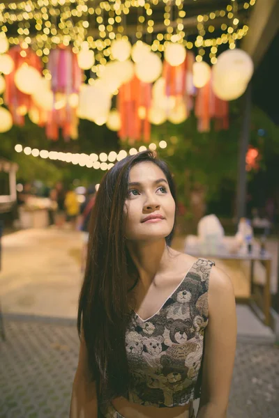 Jonge mooie Aziatische vrouw denken tegen schilderachtige uitzicht op lichtlantaarns bij de ingang van open live band in de avondmarkt van Hua Hin Thailand — Stockfoto