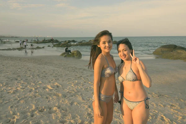Deux jeunes femmes asiatiques heureuses et belles souriantes et posant tout en donnant un signe de paix sur la plage publique de Hua Hin en Thaïlande — Photo