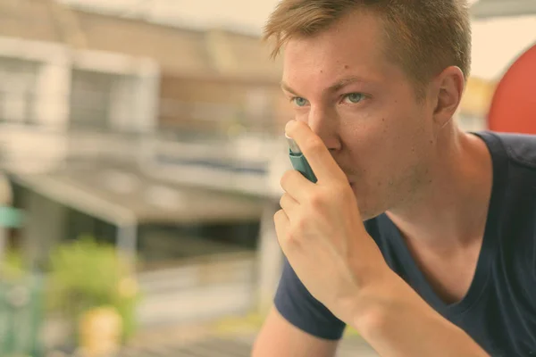 Νεαρός όμορφος άντρας που χρησιμοποιεί συσκευή εισπνοής άσθματος στο σπίτι — Φωτογραφία Αρχείου