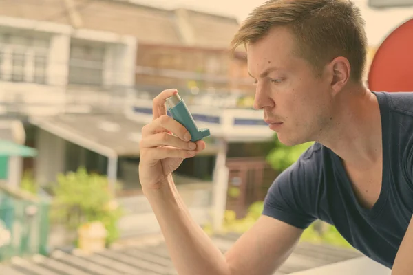 Young handsome man using asthma inhaler at home — Stock Photo, Image
