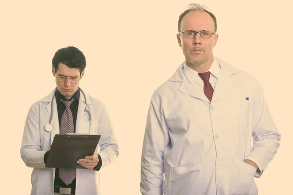 Mature man doctor with young man doctor writing on clipboard