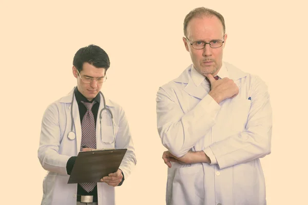 Mature man doctor thinking with young man doctor writing on clipboard