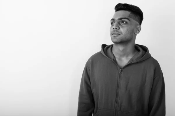 Studio shot of young Indian man wearing hoodie against white background in black and white