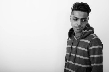 Siyah ve beyaz arka planda beyaz kapüşonlu genç Hintli adamın stüdyo fotoğrafı.