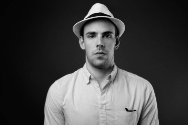 Siyah-beyaz gri arka planda şapka takan genç ve yakışıklı turistin stüdyo fotoğrafı.