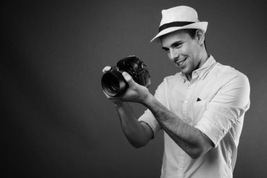 Siyah-beyaz gri arka planda şapka takan genç ve yakışıklı turistin stüdyo fotoğrafı.
