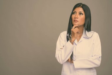 Olgun, güzel Asyalı kadın doktorun gri arka planda çekilmiş bir fotoğrafı.