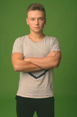 Stüdyoda, yeşil arka planda gri tişört giyen yakışıklı bir genç var.