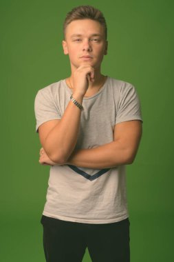 Stüdyoda, yeşil arka planda gri tişört giyen yakışıklı bir genç var.