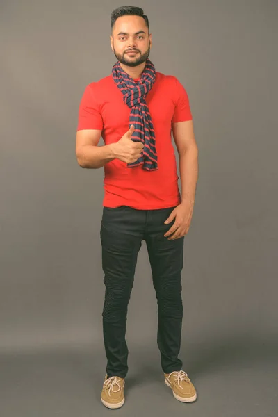 Studio shot of young bearded Indian man against gray background