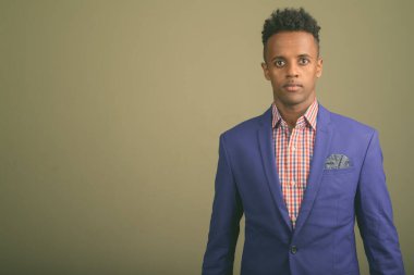 Renkli arka planda takım elbise giyen genç ve yakışıklı Afrikalı işadamının stüdyo fotoğrafı.