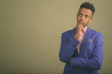 Renkli arka planda takım elbise giyen genç ve yakışıklı Afrikalı işadamının stüdyo fotoğrafı.