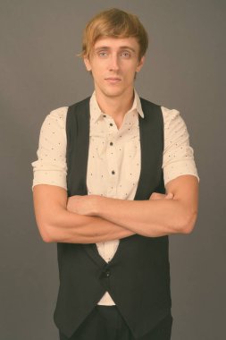 Stüdyo fotoğrafı, sarı saçlı, gri arka planda genç ve yakışıklı iş adamı.