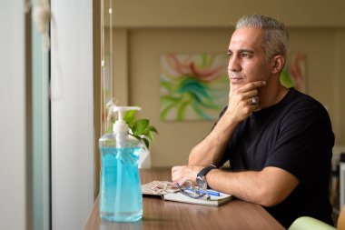 Portrait of handsome Persian man with gray hair at the library inside modern building